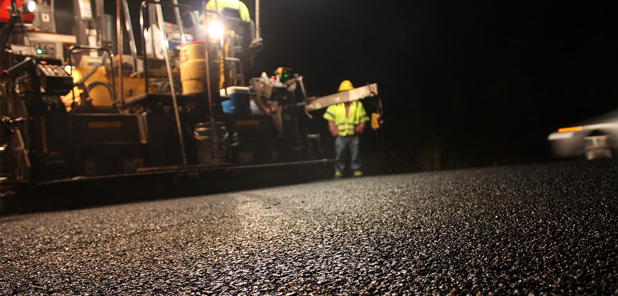 A close up of asphalt crews working on a project at night. Polymer modified asphalts