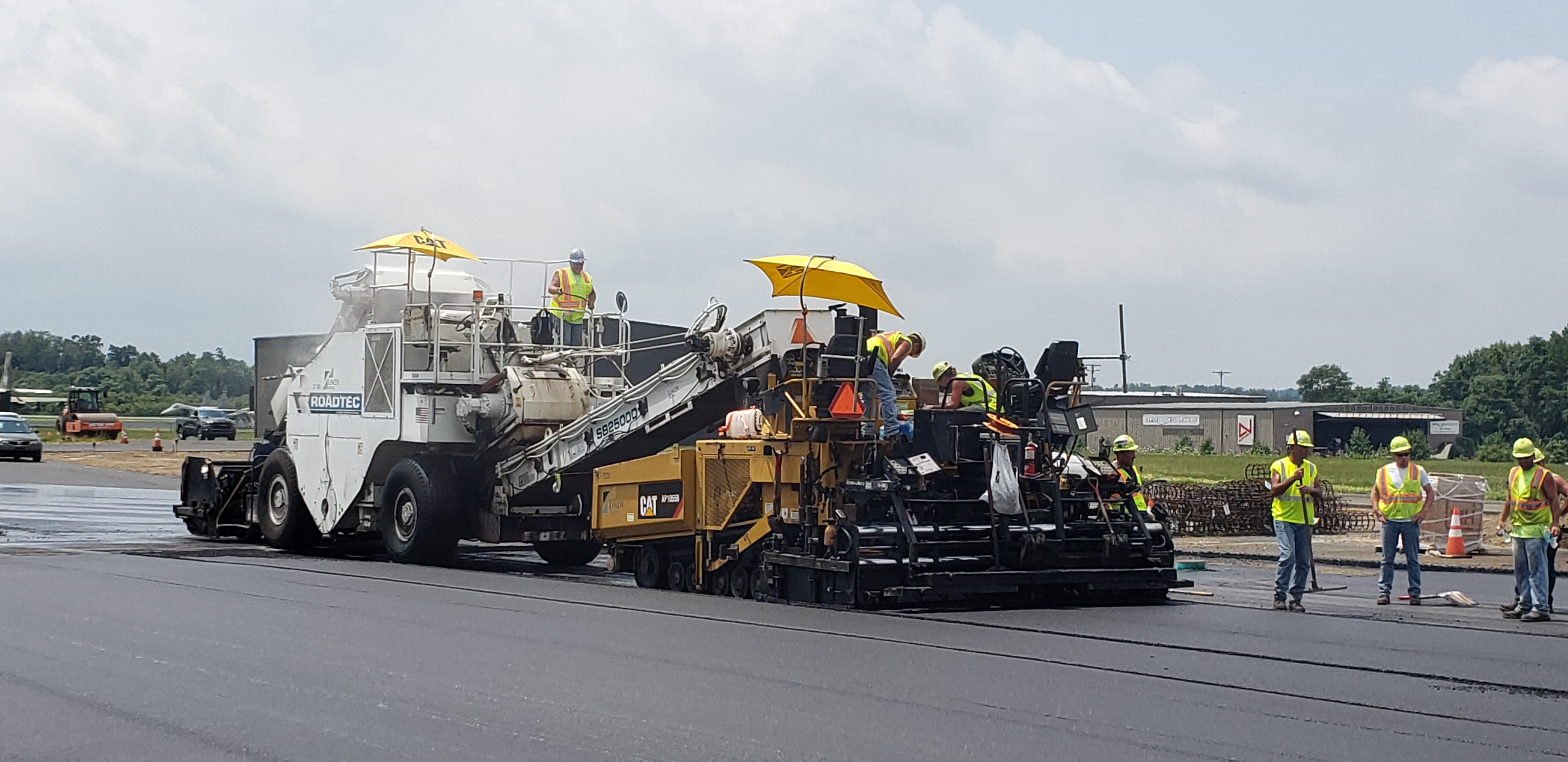 Crews in safety gear and a white and yellow asphalt equipment repaving a portion of Beaver County Airpot's tarmac.