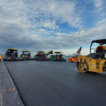 A group of asphalt rollers and construction equipment working on a airport tarmac.