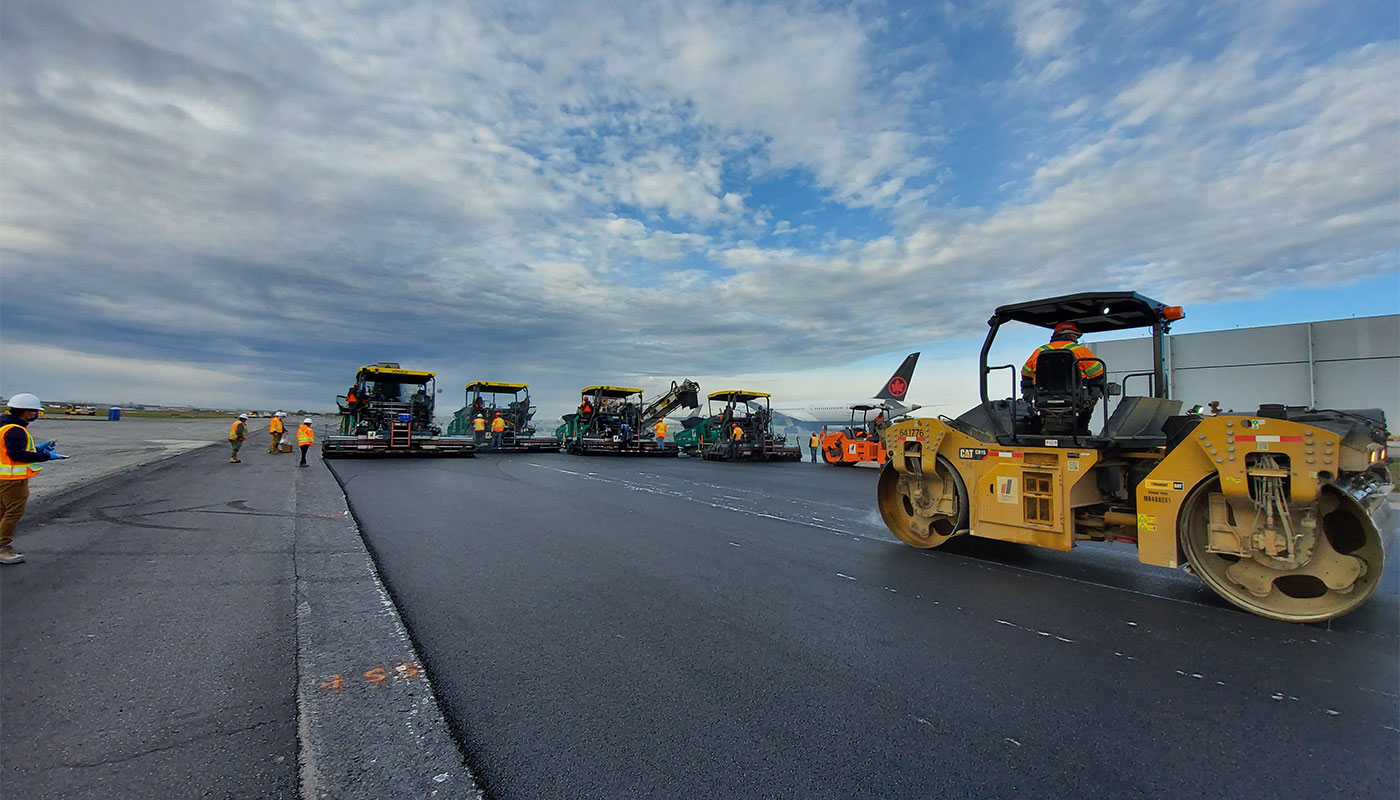 A group of asphalt rollers and construction equipment working on a airport tarmac.