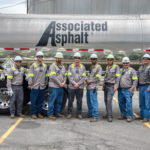 A group of field workers standing in front of a tanker with Associated Asphalts' logo.