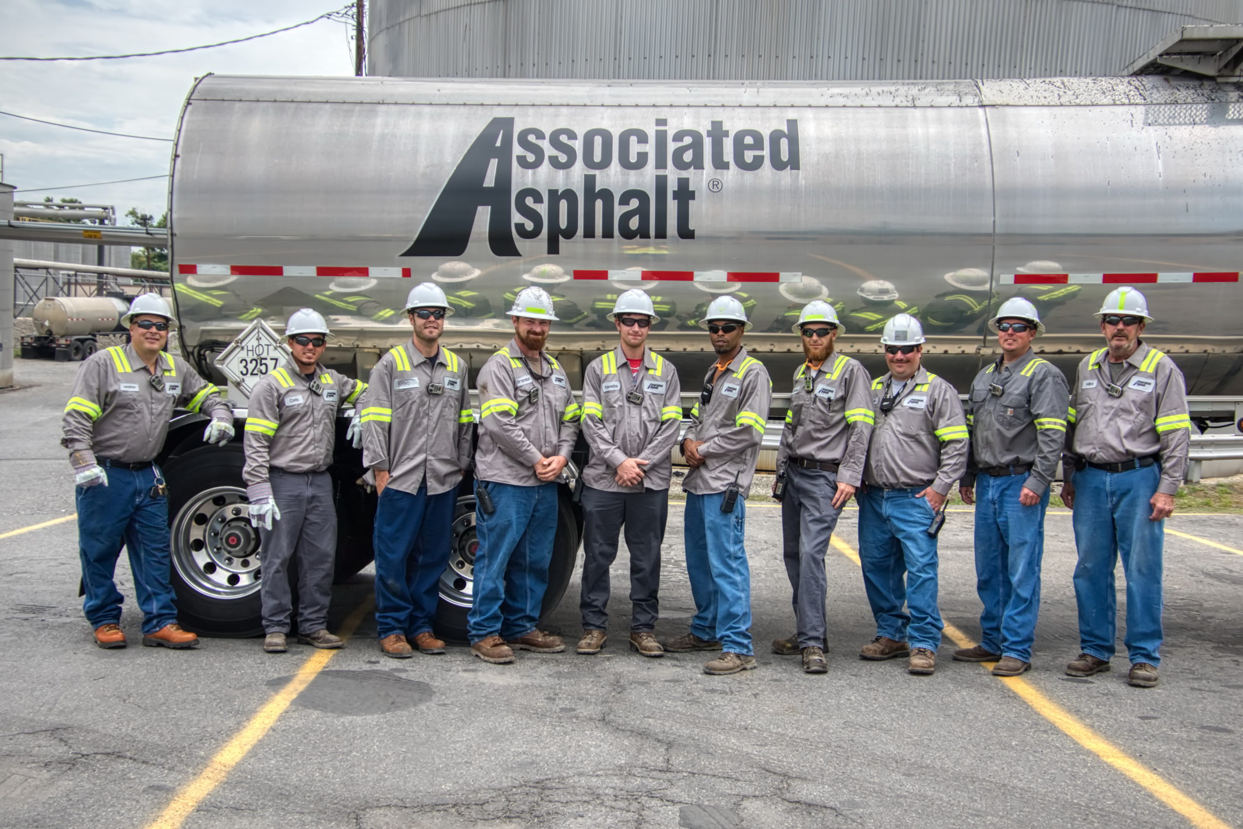 A group of field workers standing in front of a tanker with Associated Asphalts' logo.