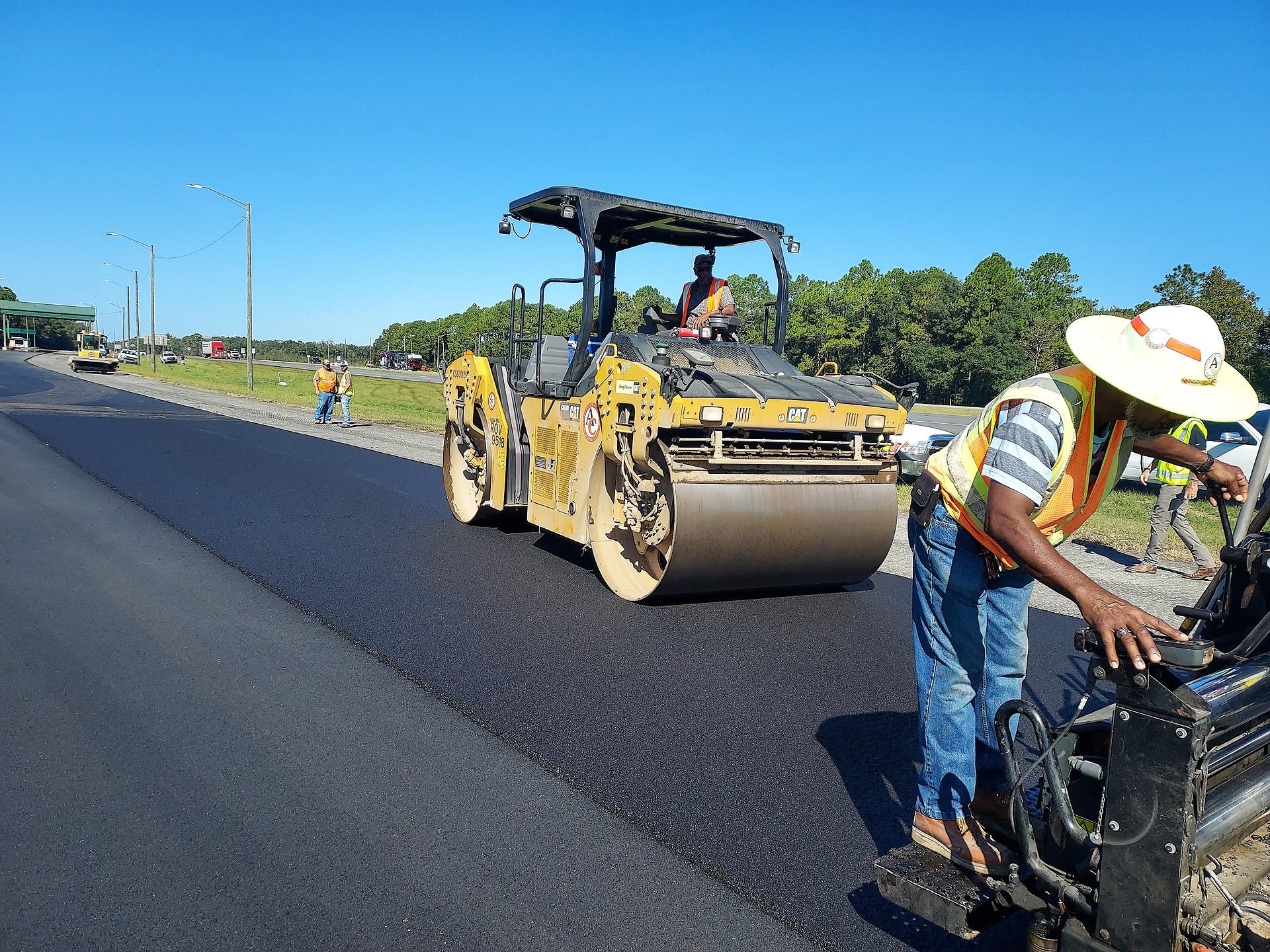 Associated Asphalt employees applying fuel resistant asphalt on a I-10 highway with a large roller vehicle.