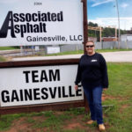 A Associated Asphalt employee smiling in front of a sign that says Team Gainesville.